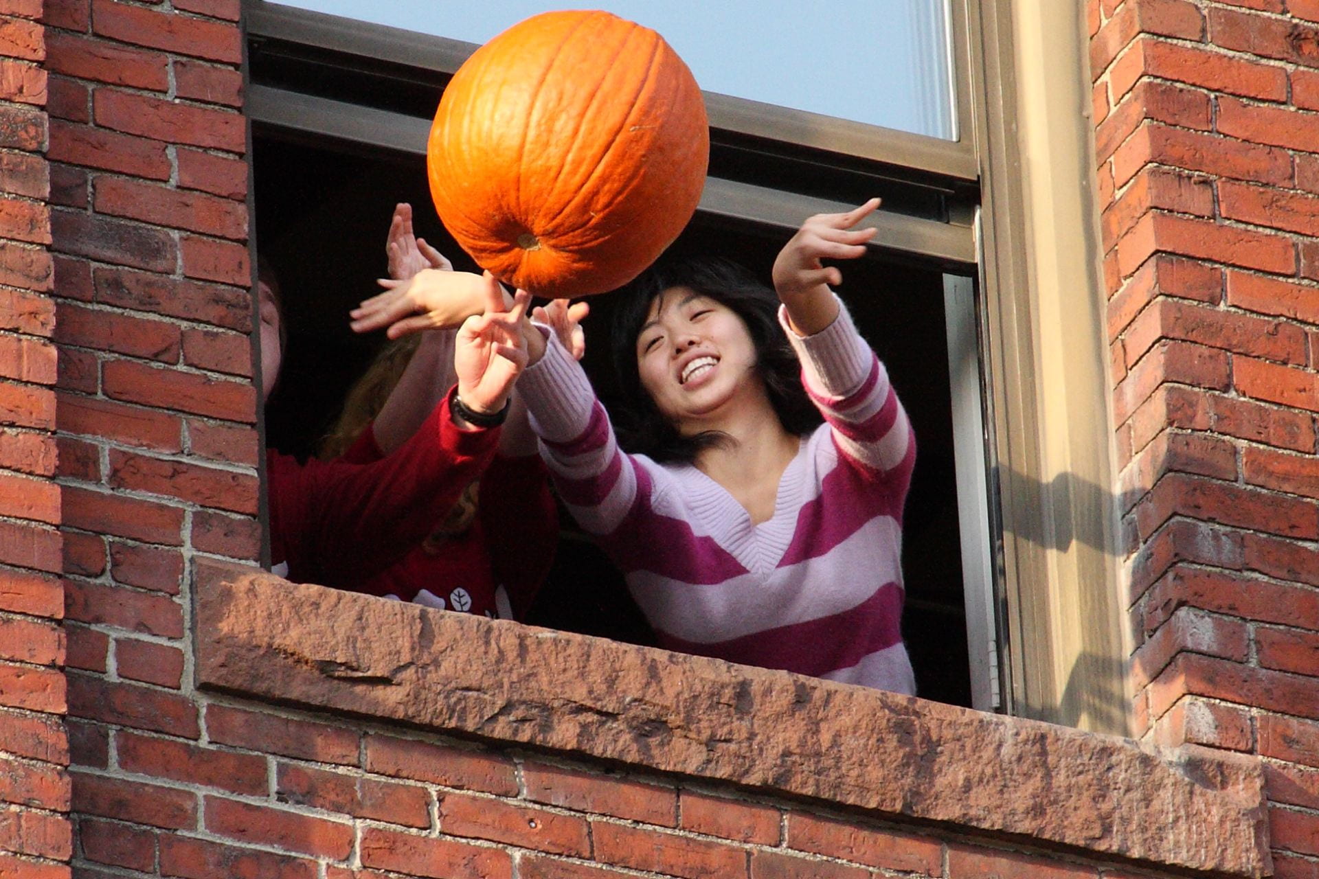 Two students toss an orange pumpkin out of a window. 