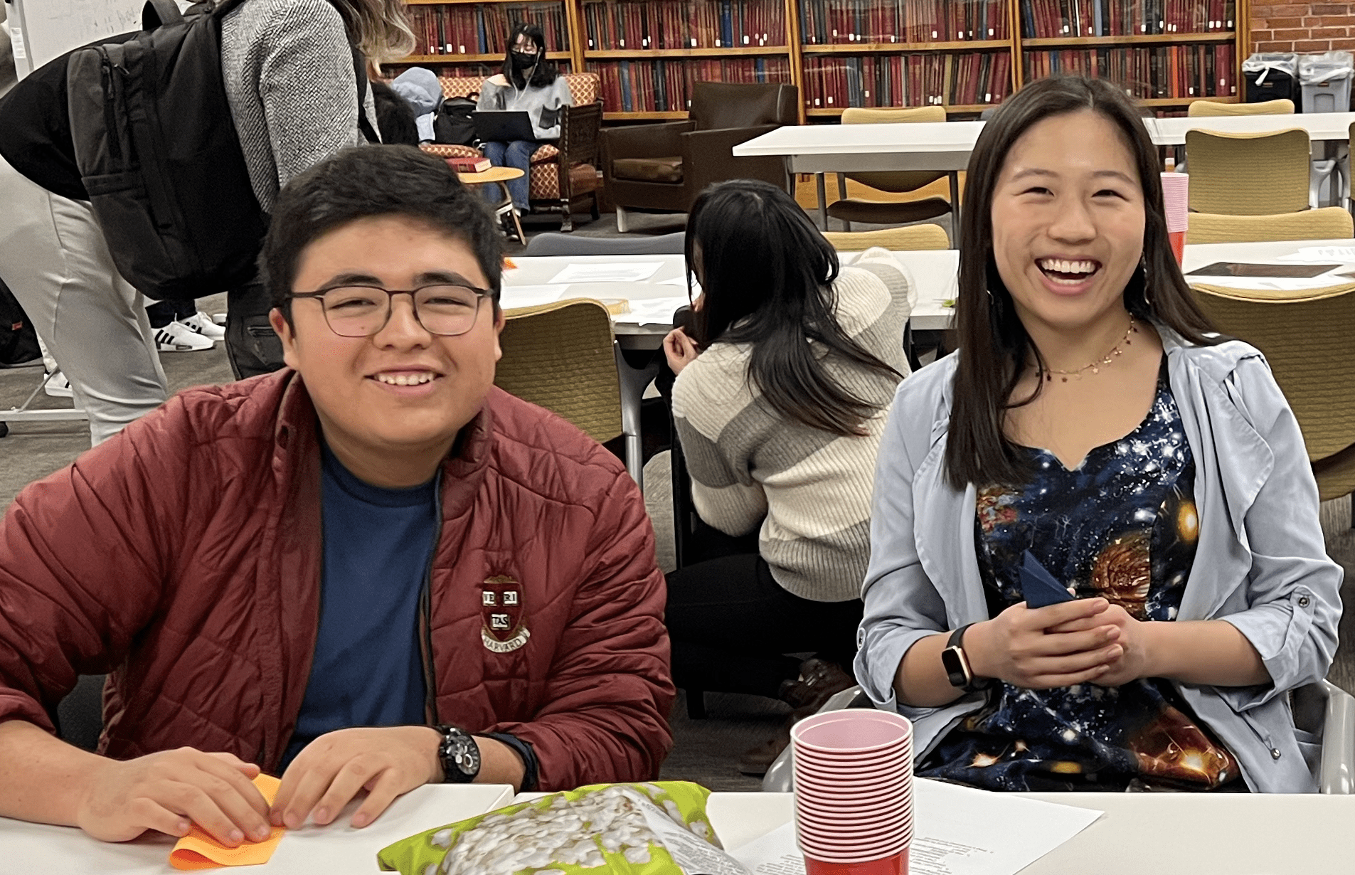Three students are sitting in the library and smiling at the camera.